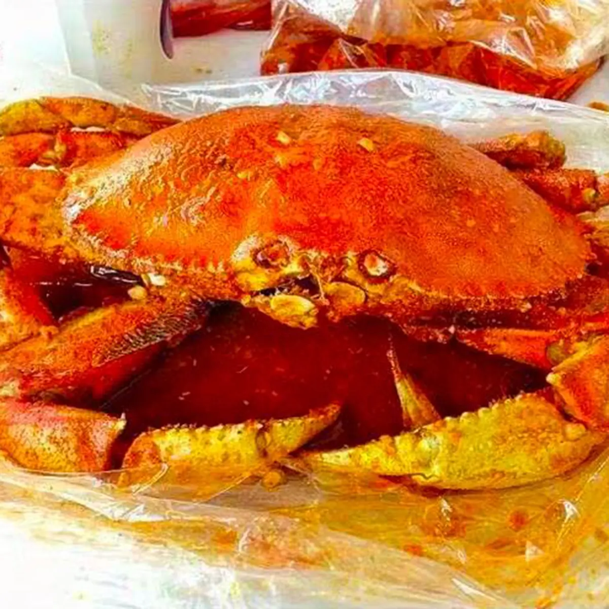 Whole seasoned dungeness crab packed in spicy boil sauce plastic bag at Red Crab Juicy Seafood, a Seafood Restaurant in Brooklyn