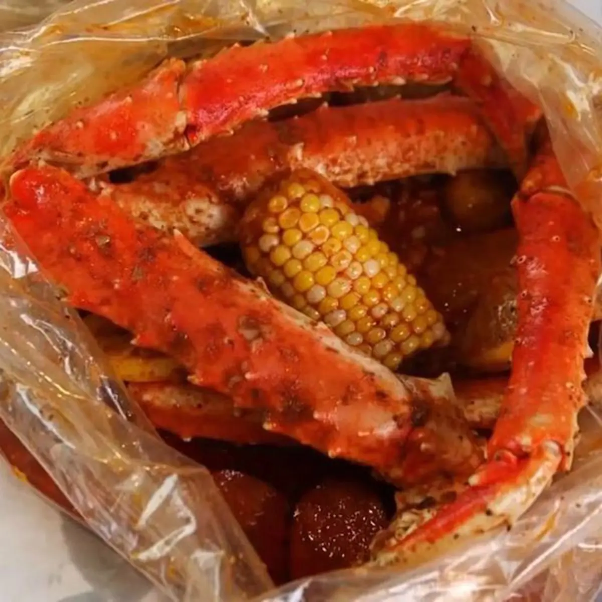 Large seasoned snow crab legs with corn potato in plastic boil bag at Red Crab Juicy Seafood, a Seafood Restaurant in Brooklyn